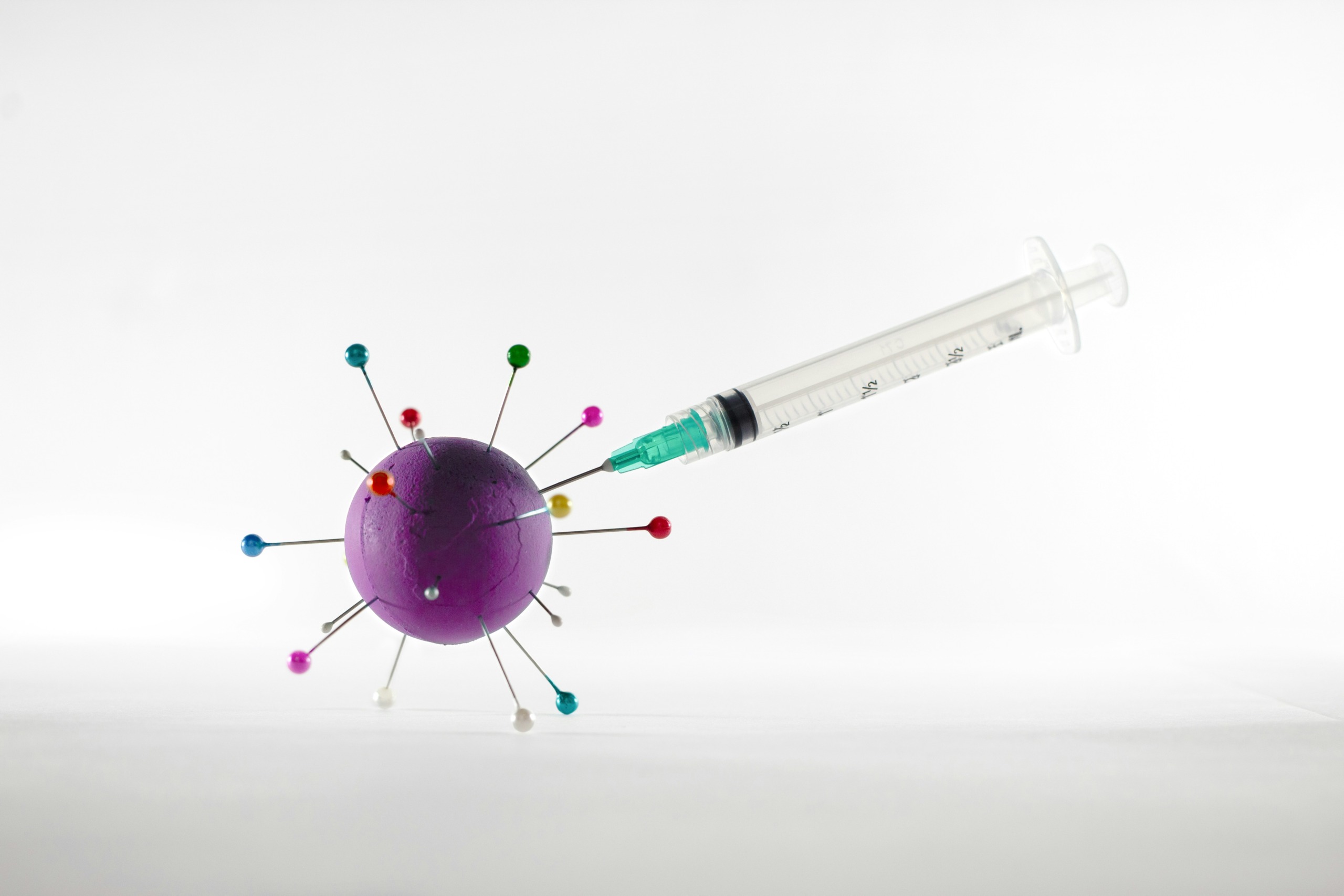 white and green syringe applying a shot on a virus representation - photo by ivan diaz